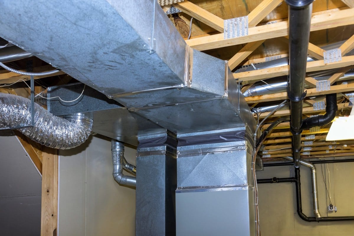 Exposed HVAC ductwork runs along a basement ceiling, showing metal vents and air distribution pipes.