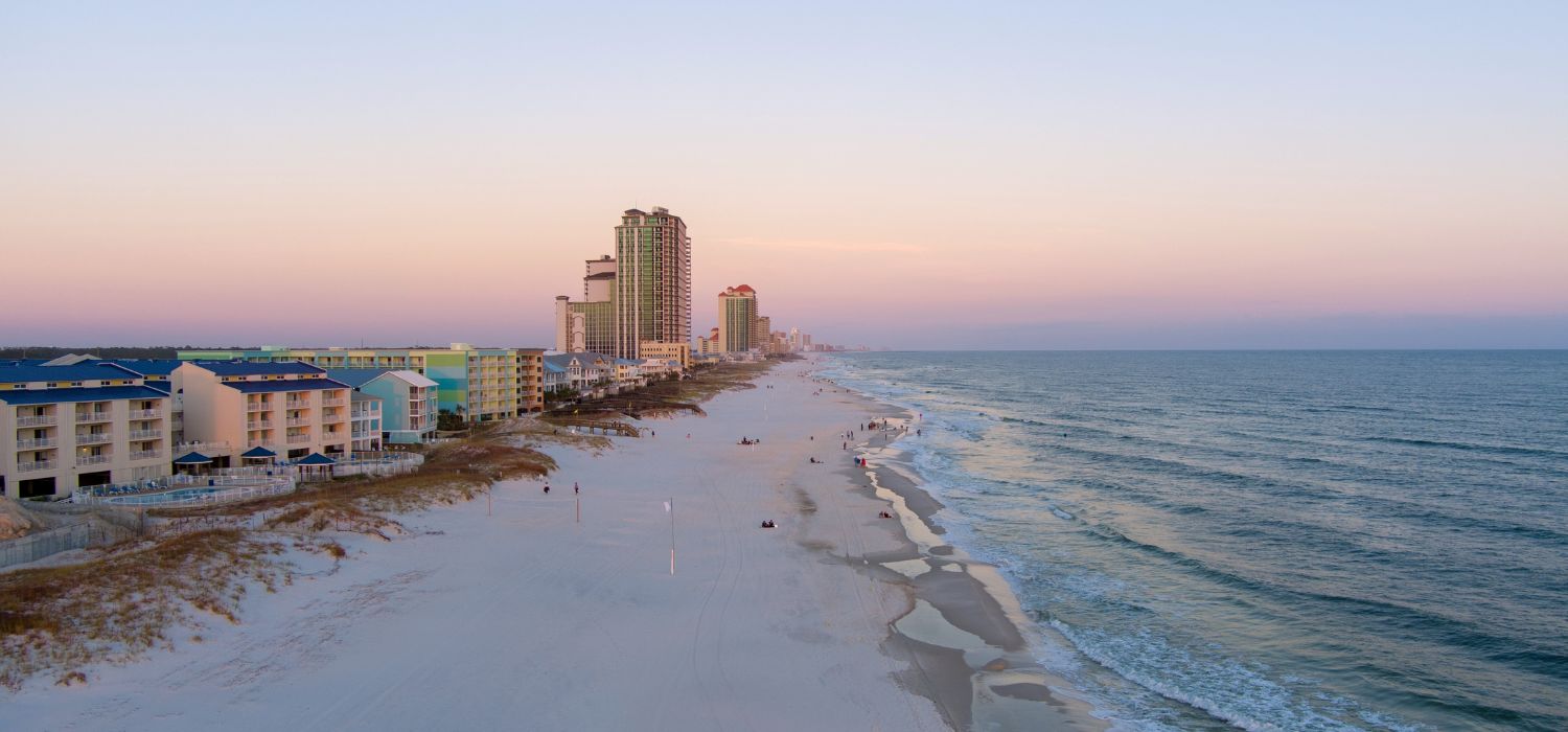 Aerial view of beachfront condos and white sand shoreline along the Gulf Coast in Orange Beach, Alabama at sunset.