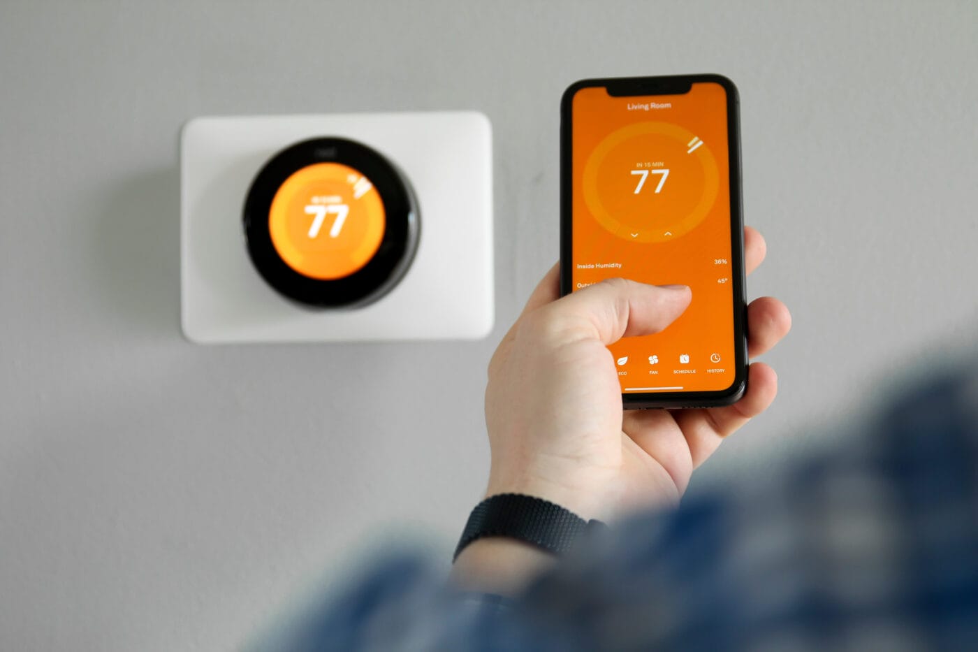 homeowner using his smartphone to change the temperature on a smart thermostat